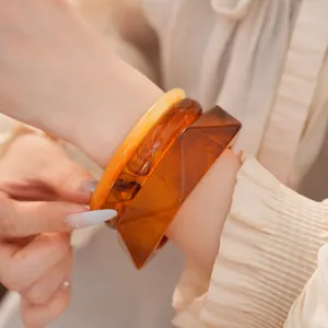 Vue rapprochée de bracelets en résine superposés aux tons chauds ambre et jaune éclatant.