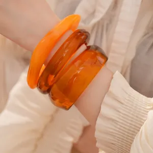 Détail de gros bracelets joncs irréguliers en résine ambre et orange sur un poignet