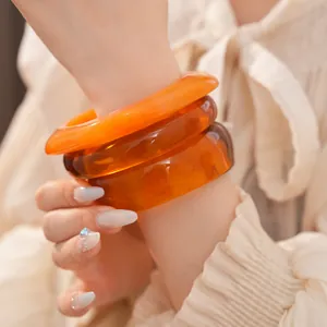 Gros plan de trois bracelets géométriques en résine ambrée portés sur un poignet en chemise