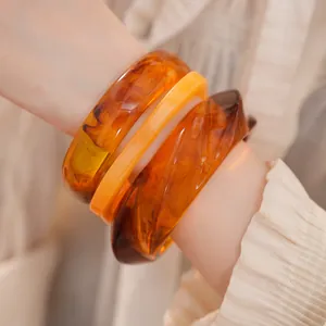 Gros plan de trois bracelets géométriques en résine ambre et orange sur un poignet de mannequin