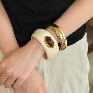 Detalle de brazalete vintage de acrílico con gema y pulsera dorada gruesa en la muñeca.
