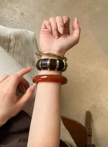 Primer plano detallado de brazaletes vintage apilados de acrílico y oro en la muñeca.