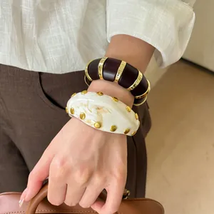 Vista detallada de brazalete vintage de acrílico jaspeado con tachuelas doradas.
