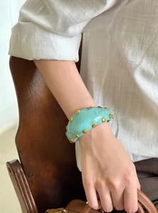 Primer plano detallado de un brazalete vintage de acrílico turquesa con tachuelas doradas