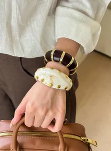 Detalle de brazaletes de acrílico vintage con bandas metálicas y tachuelas doradas