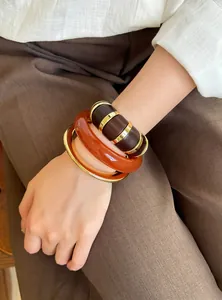 Vista detallada de pulseras vintage de acrílico y tonos dorados superpuestas en la muñeca