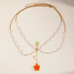 Detailed view of multilayered gold body chain with pearls and orange flower pendant