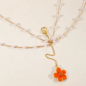 Detail view of a gold multi-layer body chain with pearls and vibrant orange flower