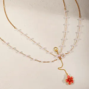 Close-up detail of a gold layered body chain featuring white pearls and a pink flower pendant