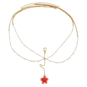 Detail of a multi-layered gold body chain with delicate white pearls and a red flower charm.