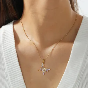 Détail soigné d'un collier pendentif papillon violet avec perles sur chaîne dorée.