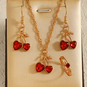 Macro detail of a cherry jewelry set featuring red heart crystals and gold-toned plating