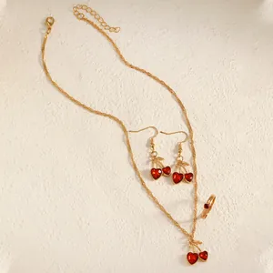 Red heart cherry jewelry set with necklace earrings and ring on textured background