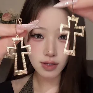 Close-up of model holding large gold hollow cross earrings with textured finish