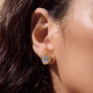 Detailed close-up of a heart-shaped gold stud earring with a clear zirconia stone on ear