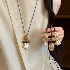 Detail of ethnic style long necklace with star and droplet charms on brown cord.