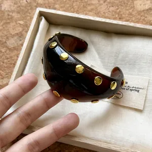 Detalle de un brazalete retro de acrílico ámbar con tachuelas de metal dorado