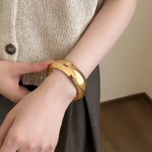 Gros plan d'un bracelet jonc large en acrylique doré vintage sur un poignet féminin