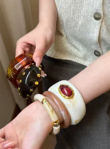 Primer plano de brazaletes de acrílico vintage bohemios con detalles dorados y gema.