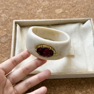 Primer plano de un brazalete ancho de acrílico blanco jaspeado con piedra roja de estilo retro