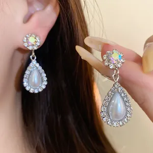 Dettaglio di eleganti orecchini a goccia color argento con perle a goccia e cristalli.