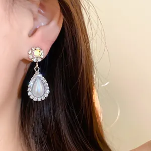 Primo piano di eleganti orecchini pendenti a goccia con strass e perle su una modella.