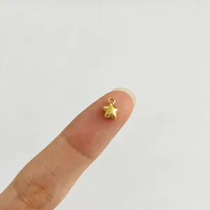Makroansicht eines kleinen goldenen Sternanhängers auf einer Fingerspitze zur Größenangabe