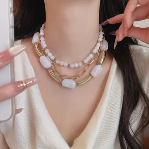 Dettaglio di una collana a più strati con perle in acrilico bianco e catene oro