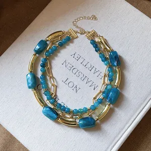Dettaglio di perle acriliche blu marmorizzate e catena d'oro su collana multistrato