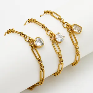 Close-up detail of gold-tone paperclip and bead chain bracelets featuring zircon charms