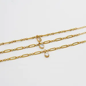 Close-up detail of gold paperclip and bead chain bracelets with heart and CZ charms
