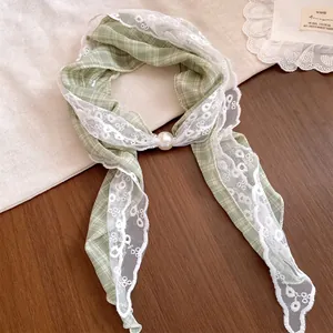 Macrodetail van een groene geruite zijden sjaalketting met witte kant en een parel.