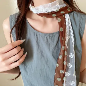 Detailweergave van bruine sjaalketting met stippen en witte bloemen kant afwerking.