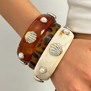 Detailed close-up of retro resin wide bangles with pearl and shell charms on model wrist