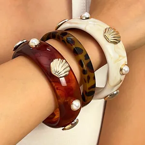 Close-up of resin bangles featuring seashell and pearl accents in amber and tortoiseshell.
