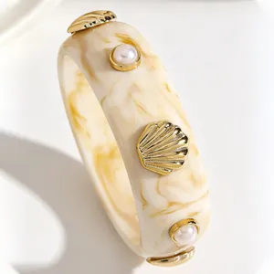 Macro detail of a wide vintage resin bangle with golden shell and pearl accents.