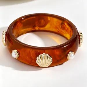 Detailed macro view of amber tortoise shell resin bangle with gold shells and pearls