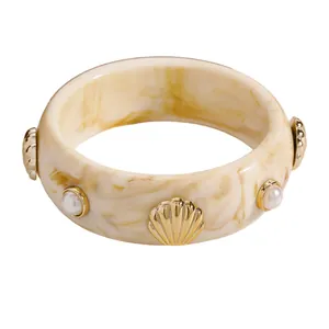 Detail view of tortoiseshell resin bangle with golden scallop and pearl accents