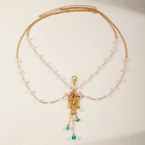 Close-up detail of a gold multi-layer body chain featuring a lobster pendant and pearls