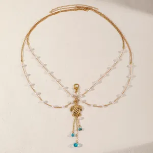 Detail shot of a multi-layer gold turtle pendant body chain with white pearls and blue beads