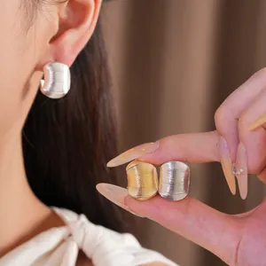 Détail de boucles d'oreilles minimalistes en forme de C avec texture en fini doré et argenté.