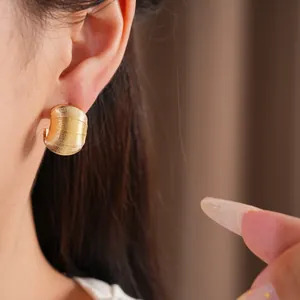 Vue détaillée d'une boucle d'oreille dorée en forme de C texturée portée sur l'oreille