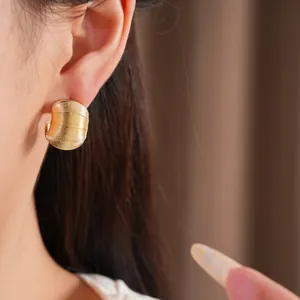 Vue détaillée de boucles d'oreilles créoles dorées en C avec finition texturée sur modèle