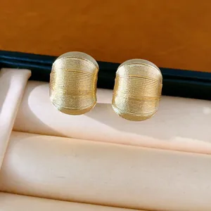 Détail macro de boucles d'oreilles dorées en forme de C avec une finition texturée