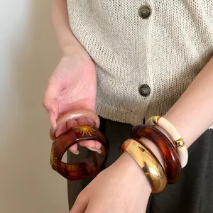 Primer plano de brazaletes de acrílico y oro de estilo vintage en la muñeca de una modelo