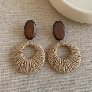 Close-up detail of boho style woven raffia hoop earrings featuring dark wooden oval tops