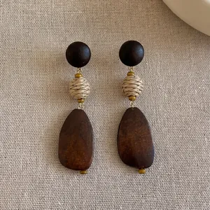 Macro detail of retro geometric wood earrings featuring woven straw bead and dark finish