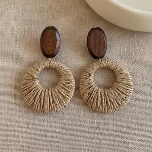 Detail shot of bohemian wooden stud and woven raffia straw round dangle earrings