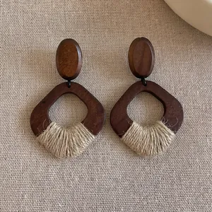 Close-up of geometric wooden earrings with woven twine detail on a rustic linen surface