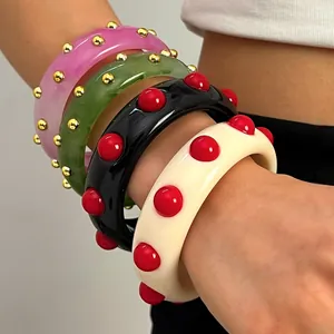 Detail view of colorful retro acrylic wide bangles with raised dots on model's arm.